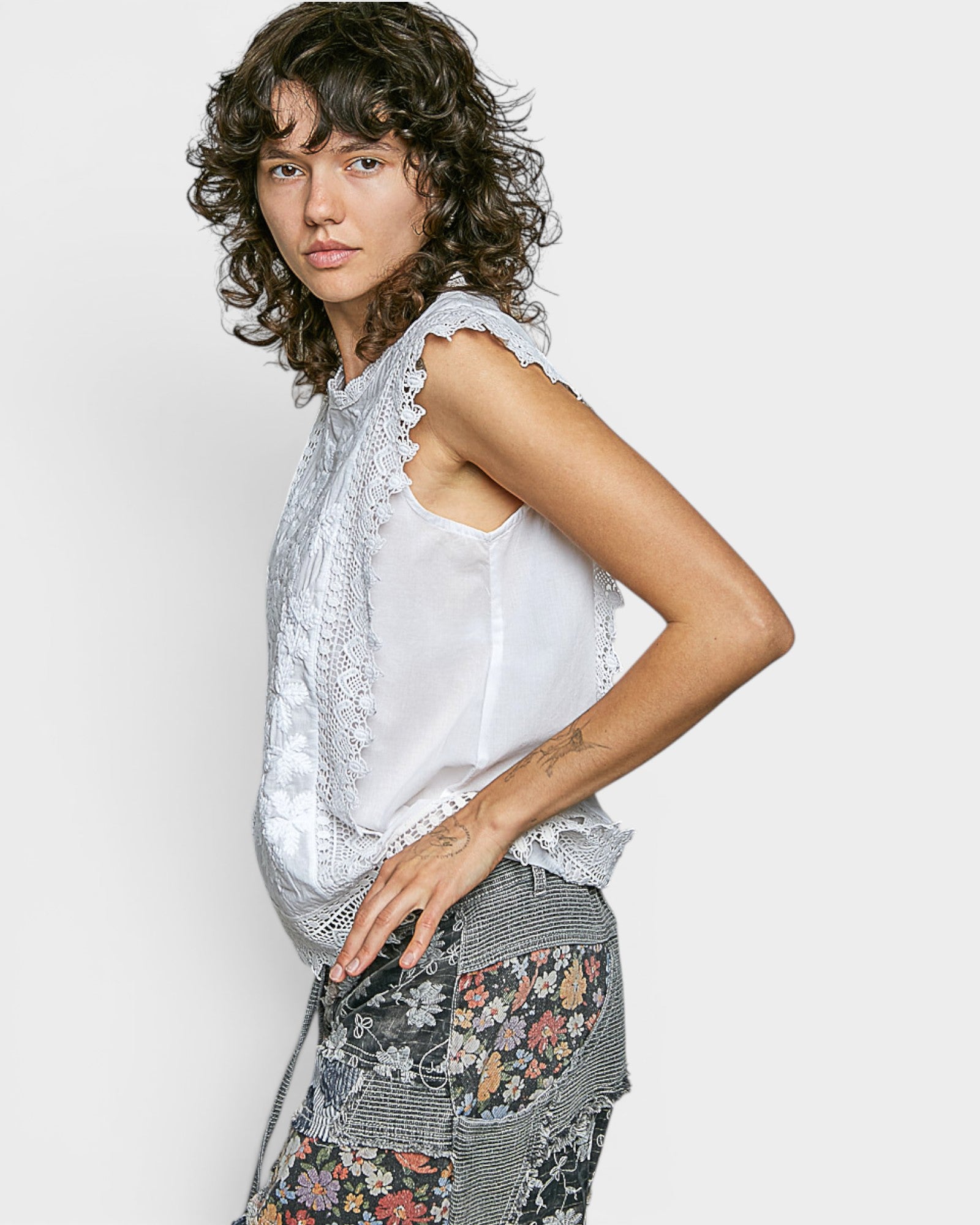 Woman wearing a sleeveless top with lace details and floral pants on a plain background