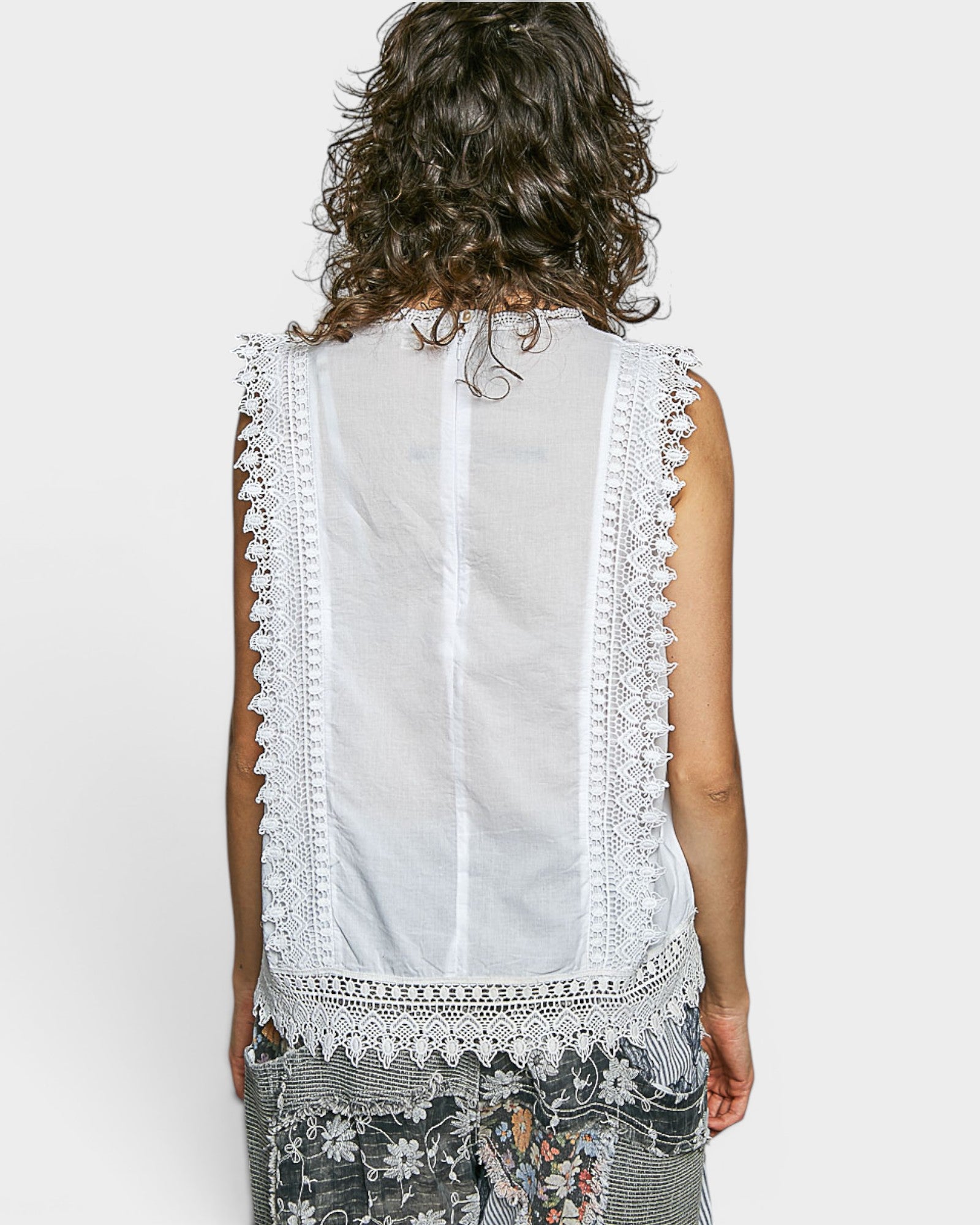 White sleeveless top with lace detailing worn by a person on a white background