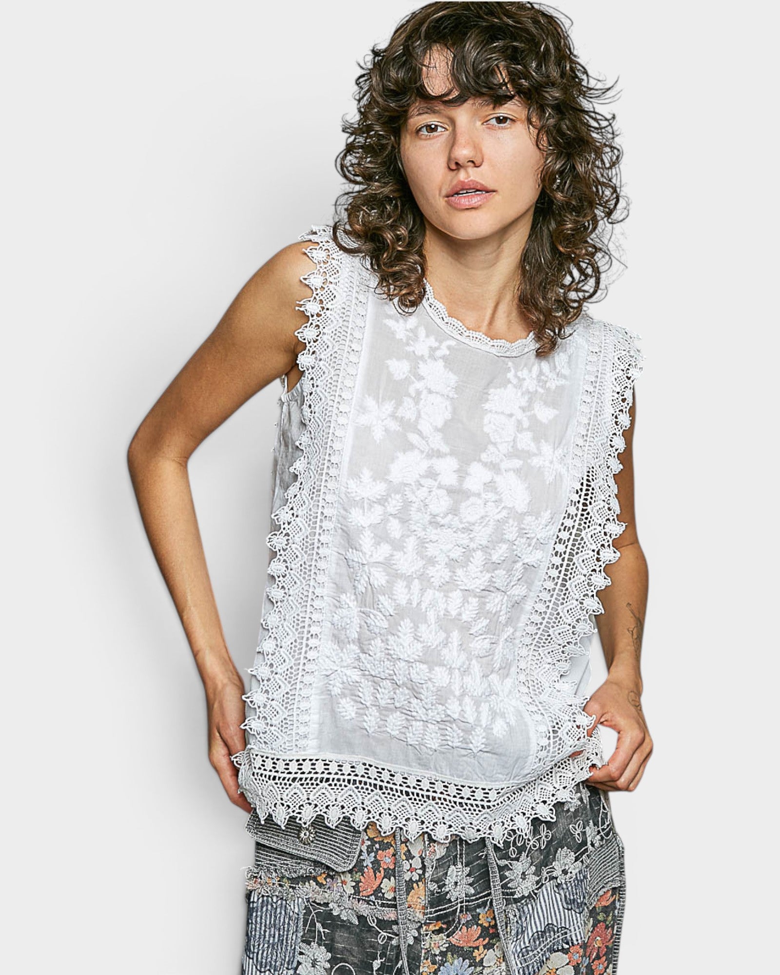 Person wearing a sleeveless top with lace details on a white background