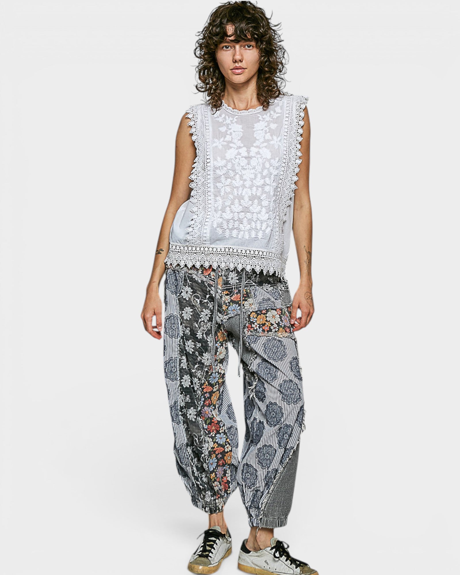 Woman wearing a white sleeveless top with lace details and patterned pants on a white background