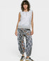 Woman wearing a white sleeveless top with lace details and patterned pants on a white background