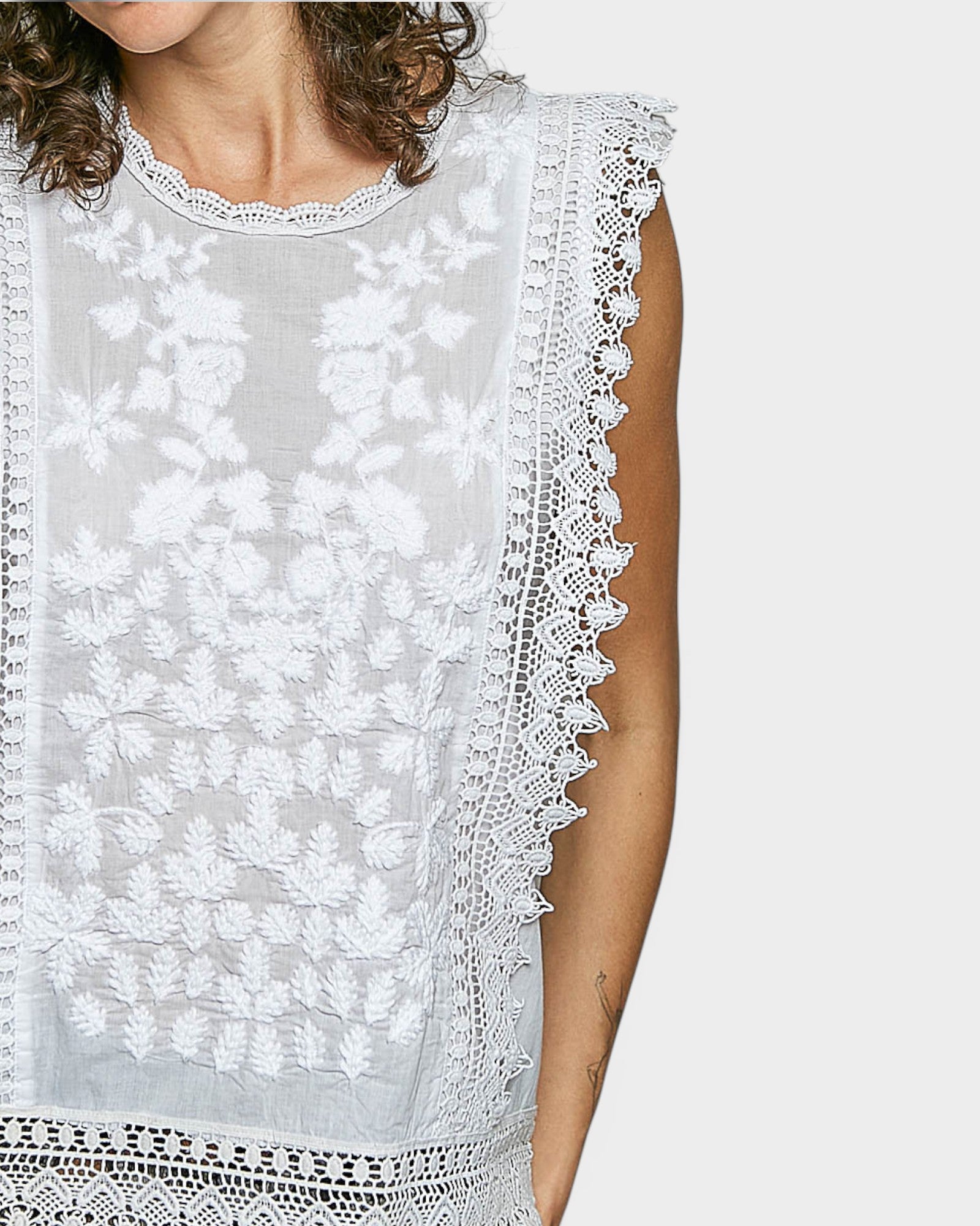 White lace-trimmed top worn by a person on a white background