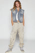 Woman wearing a denim vest, white top, beige cargo pants, and gray sneakers on a white background