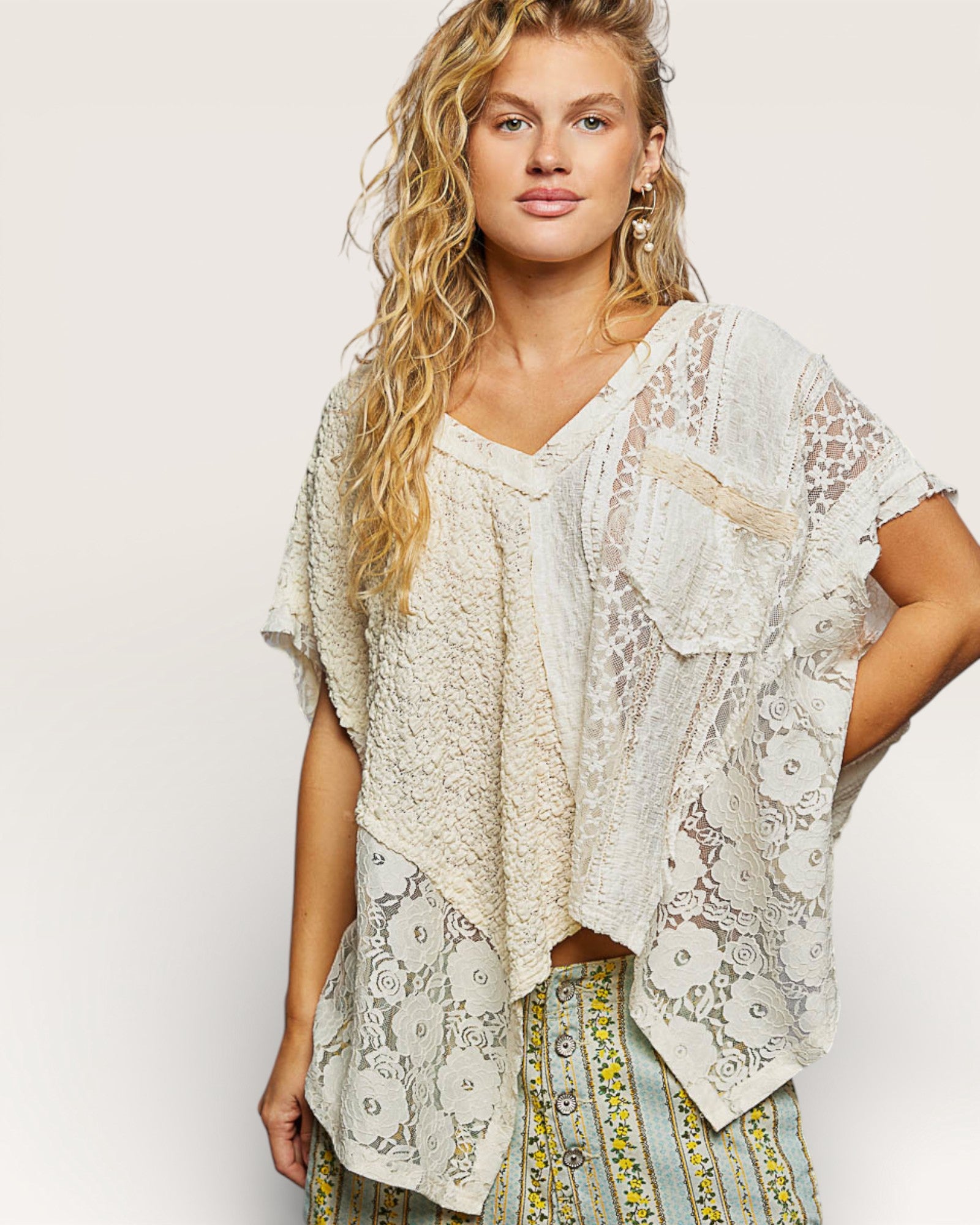 Woman wearing a lace top and patterned pants on a plain background