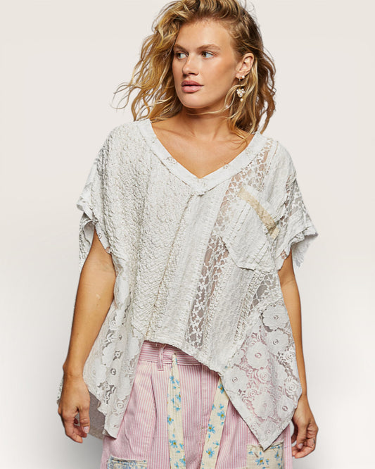 Woman wearing a light-colored lace top with a plain background