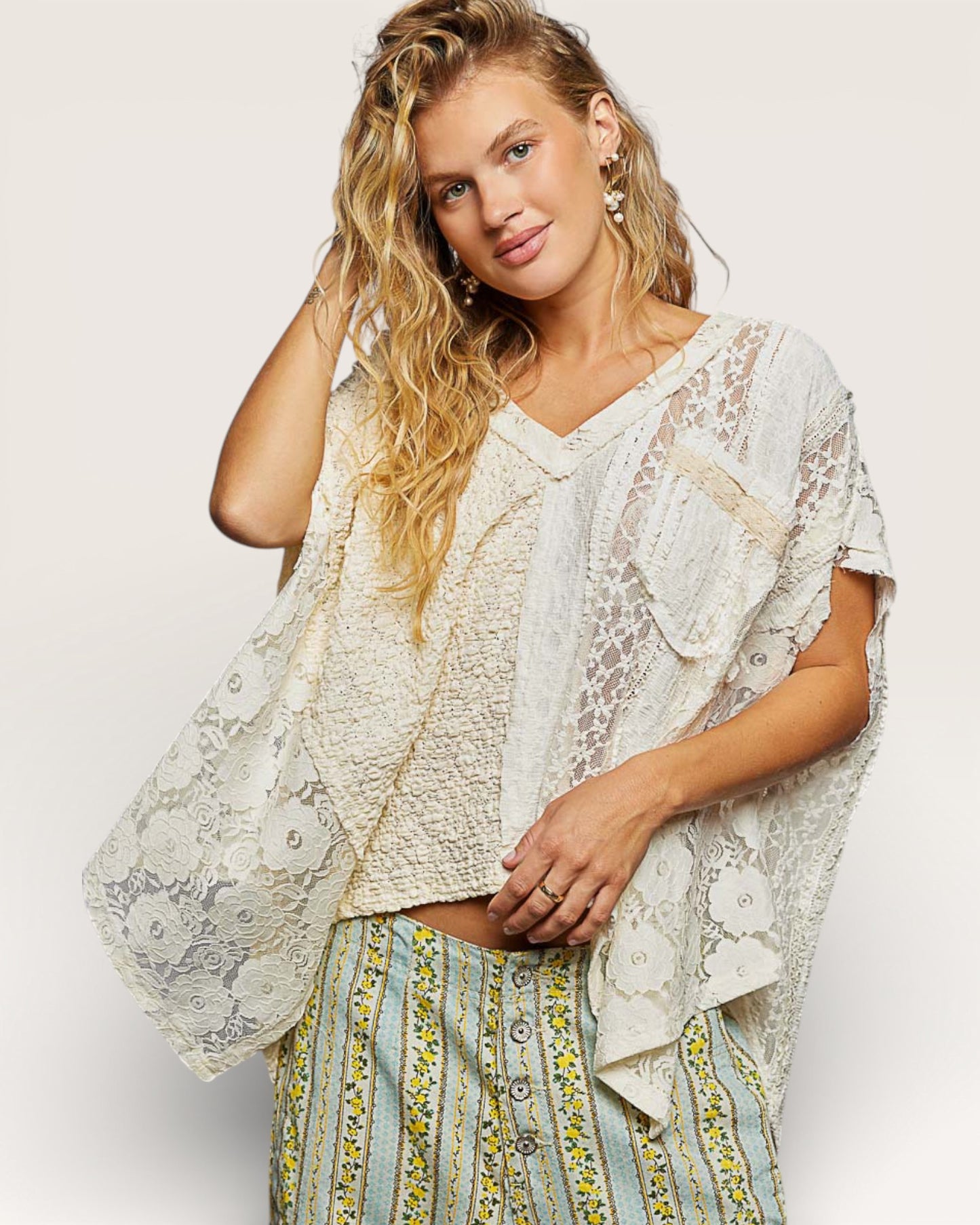 Woman wearing a light-colored lace top and patterned skirt on a plain background