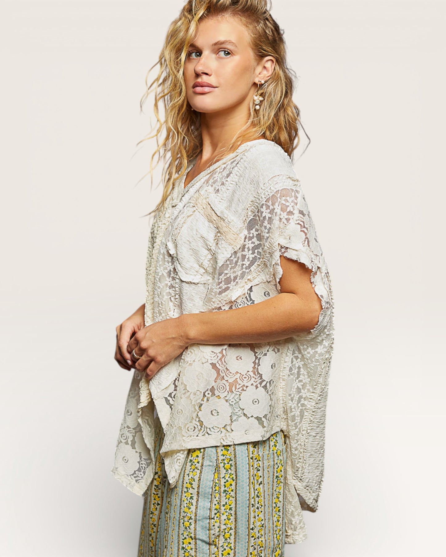 Woman wearing a light-colored lace top with a plain background