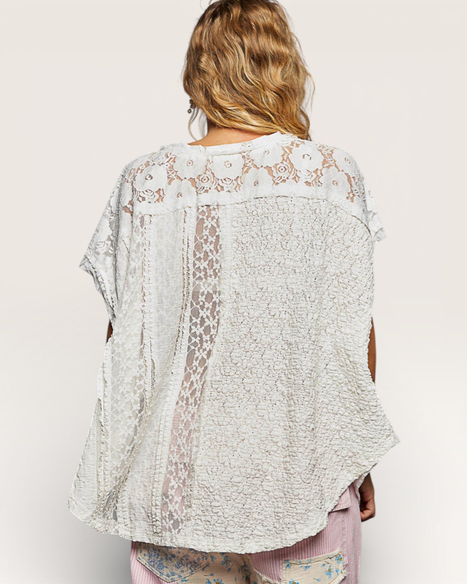 Person wearing a light-colored lace top with a plain background