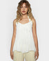 Woman wearing a white sleeveless top with ruffled straps on a plain background
