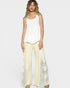 Woman wearing a white sleeveless top and cream pants with lace details on a light gray background