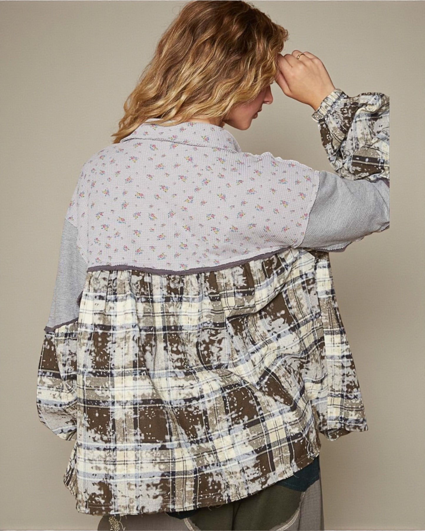 Person wearing a plaid jacket over a patterned shirt against a beige background