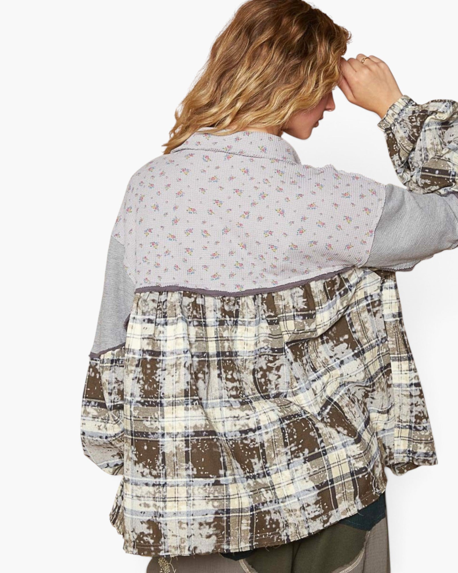 A woman shown from the back wearing a patchwork button-up shirt with a light floral yoke, gray sleeves, and a distressed brown plaid lower section, against a plain white background.