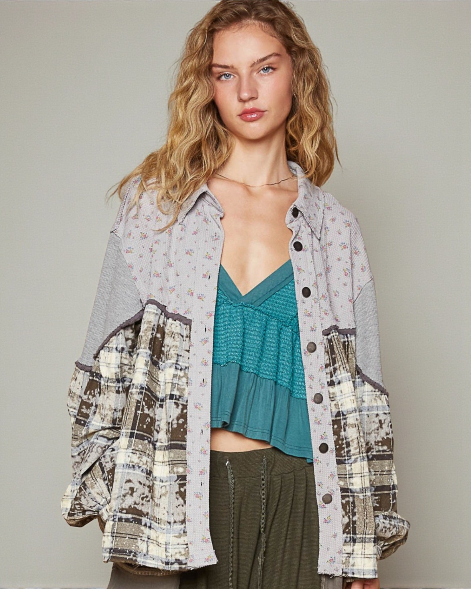 Woman wearing a patterned shirt over a teal top with a neutral background