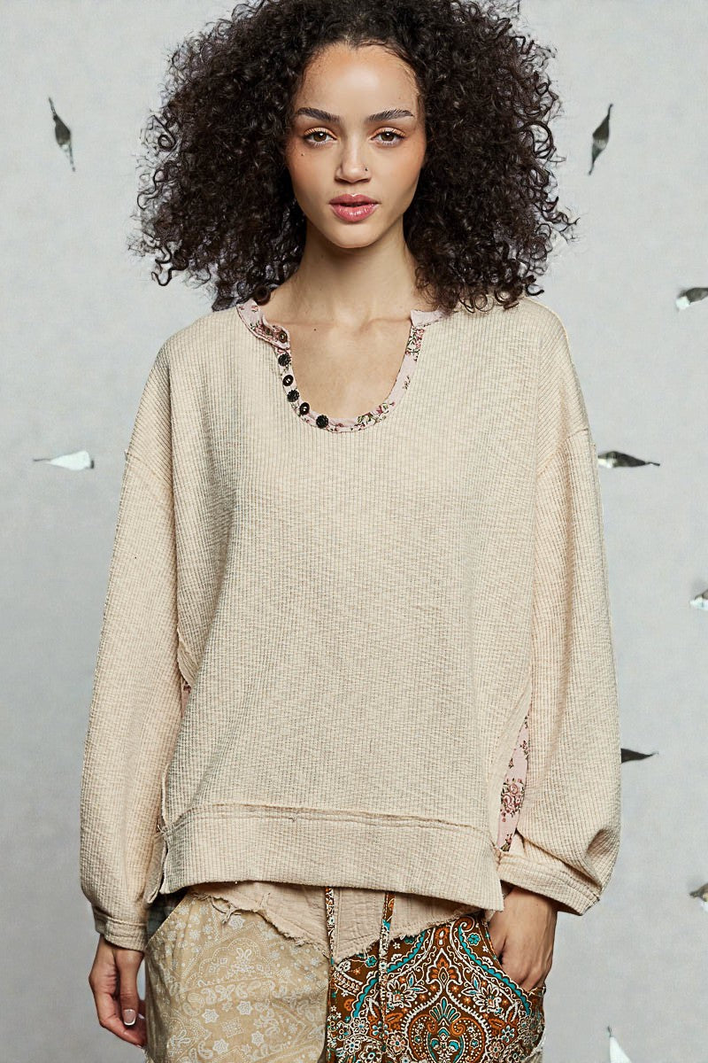 Woman wearing a beige sweater with floral details against a gray background