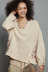 Woman wearing a beige sweater with floral patterns on a gray background