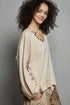 Woman wearing a beige cardigan over a patterned top against a gray background