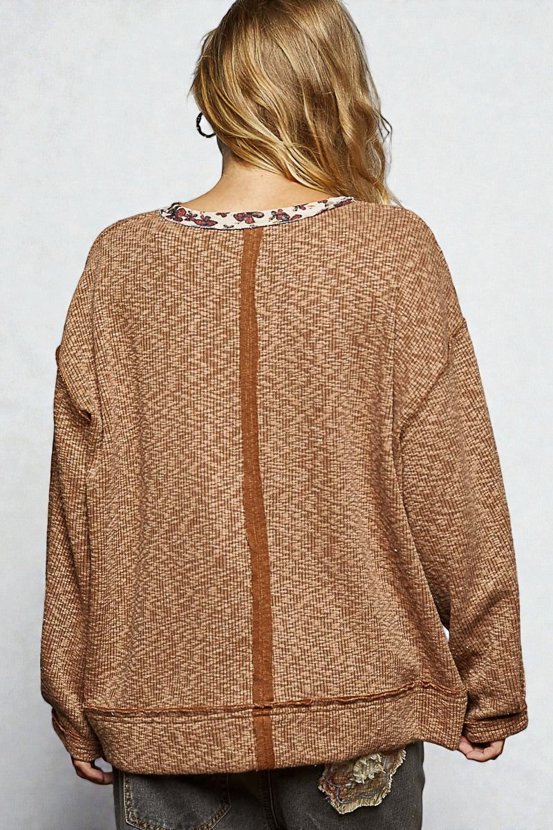 Person wearing a brown sweater with a floral pattern underneath on a white background