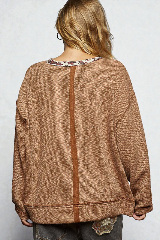 Person wearing a brown sweater with a floral pattern underneath on a white background