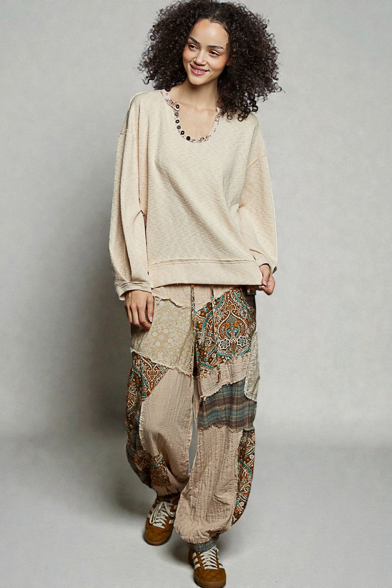 Woman wearing a beige top and patterned pants on a plain background