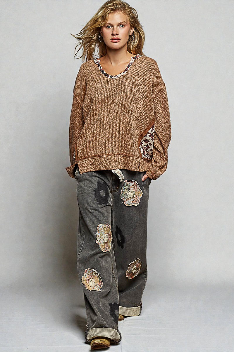 Woman wearing a brown sweater and gray pants with floral patches on a plain background