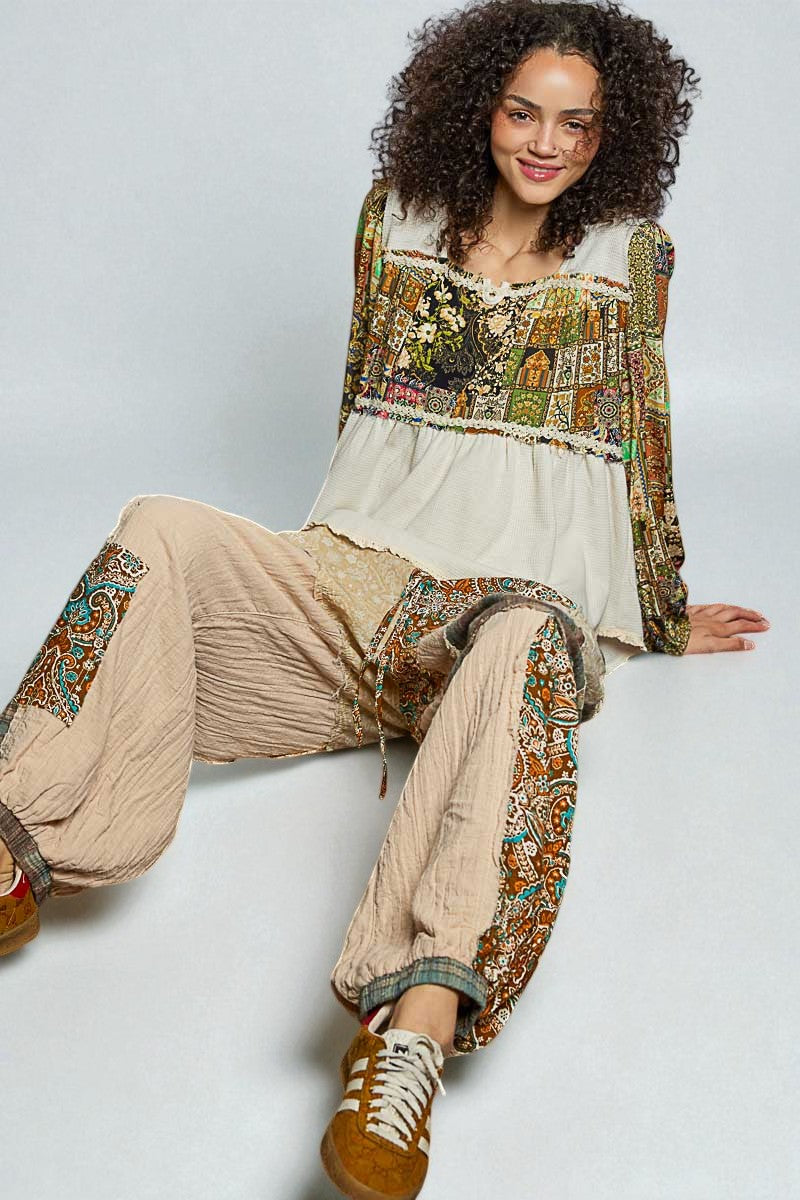 Woman wearing a bohemian-style outfit with a patterned top and beige pants on a white background