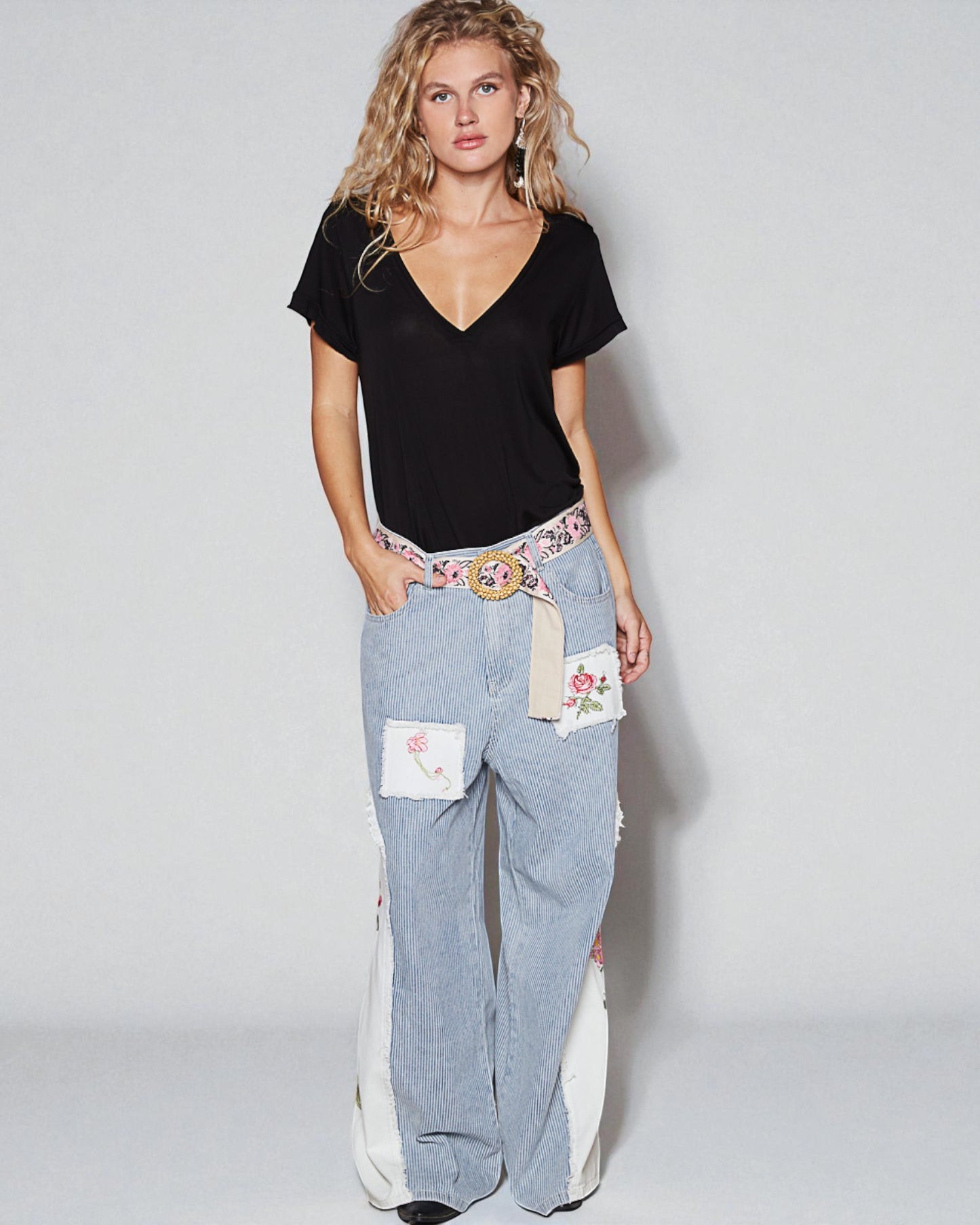 Woman wearing a black top and light blue jeans with floral patches on a white background