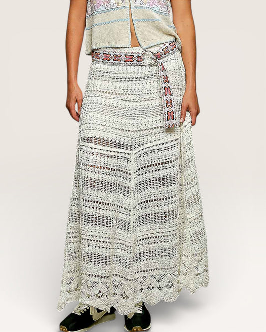 Person wearing a long, patterned skirt with a belt on a plain background