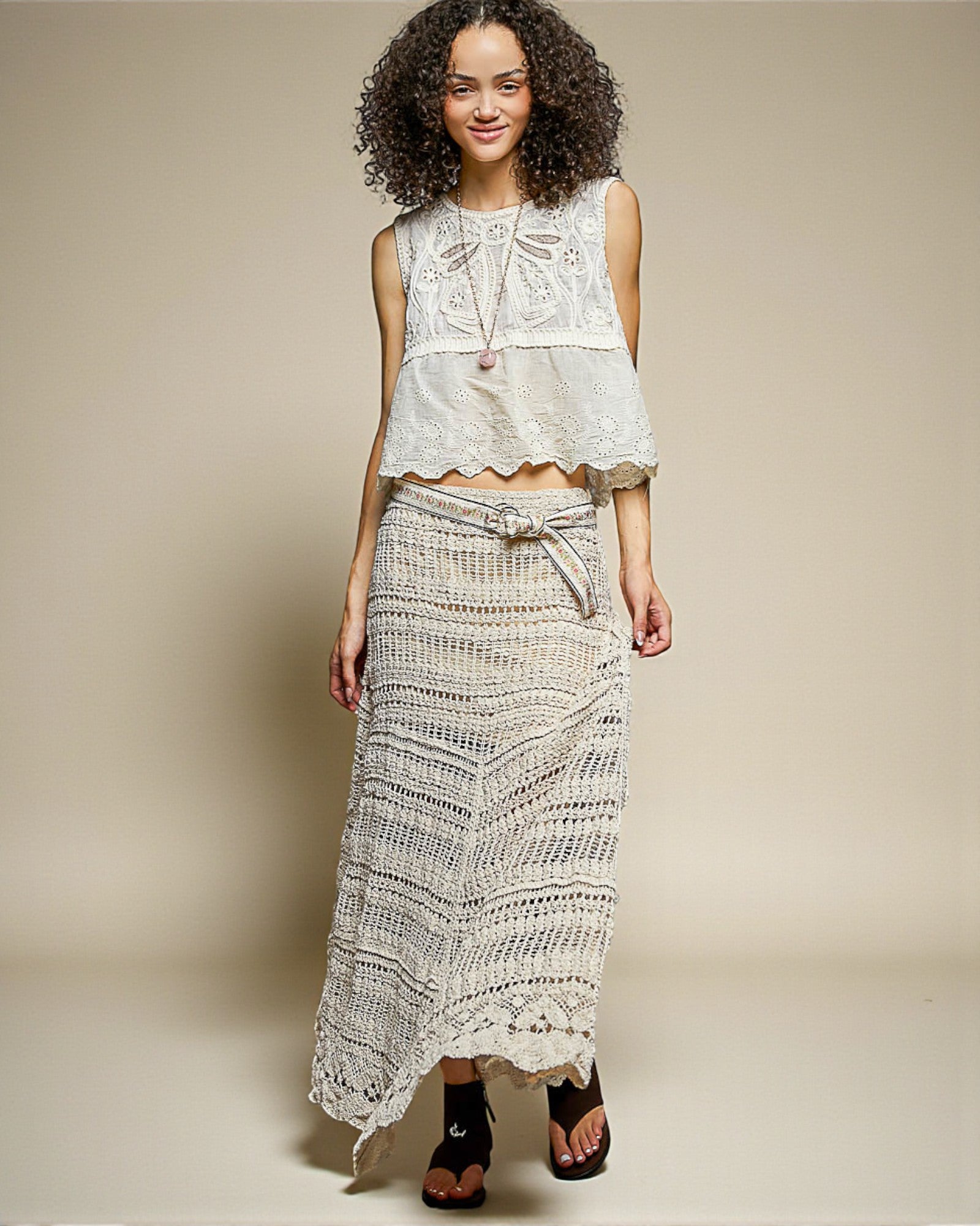 Woman wearing a white lace top and long skirt against a beige background