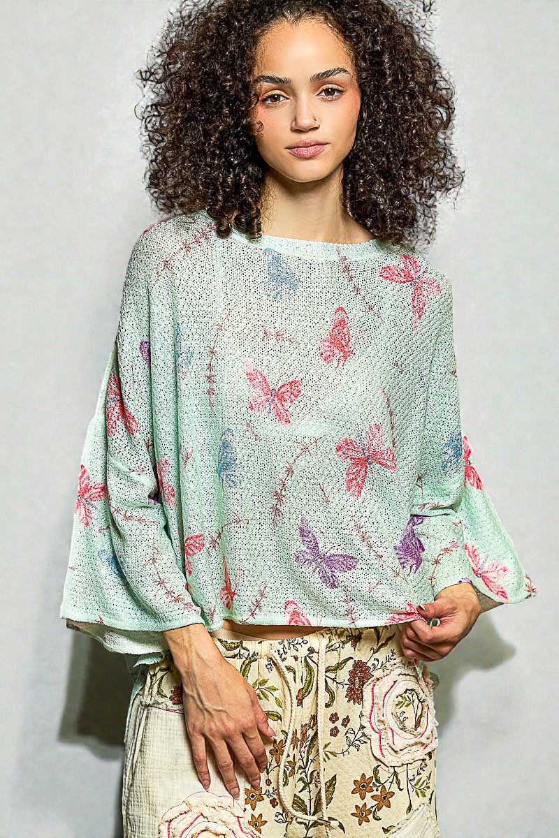 Woman wearing a light green blouse with butterfly patterns on a plain background