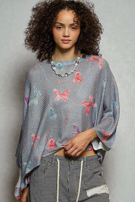 Woman wearing a gray sweater with butterfly patterns against a plain background