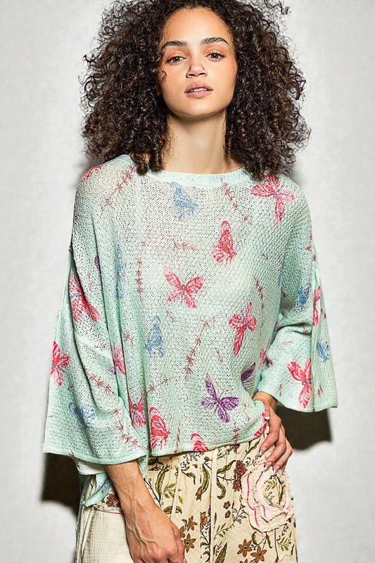 Woman wearing a light green blouse with butterfly pattern against a plain background