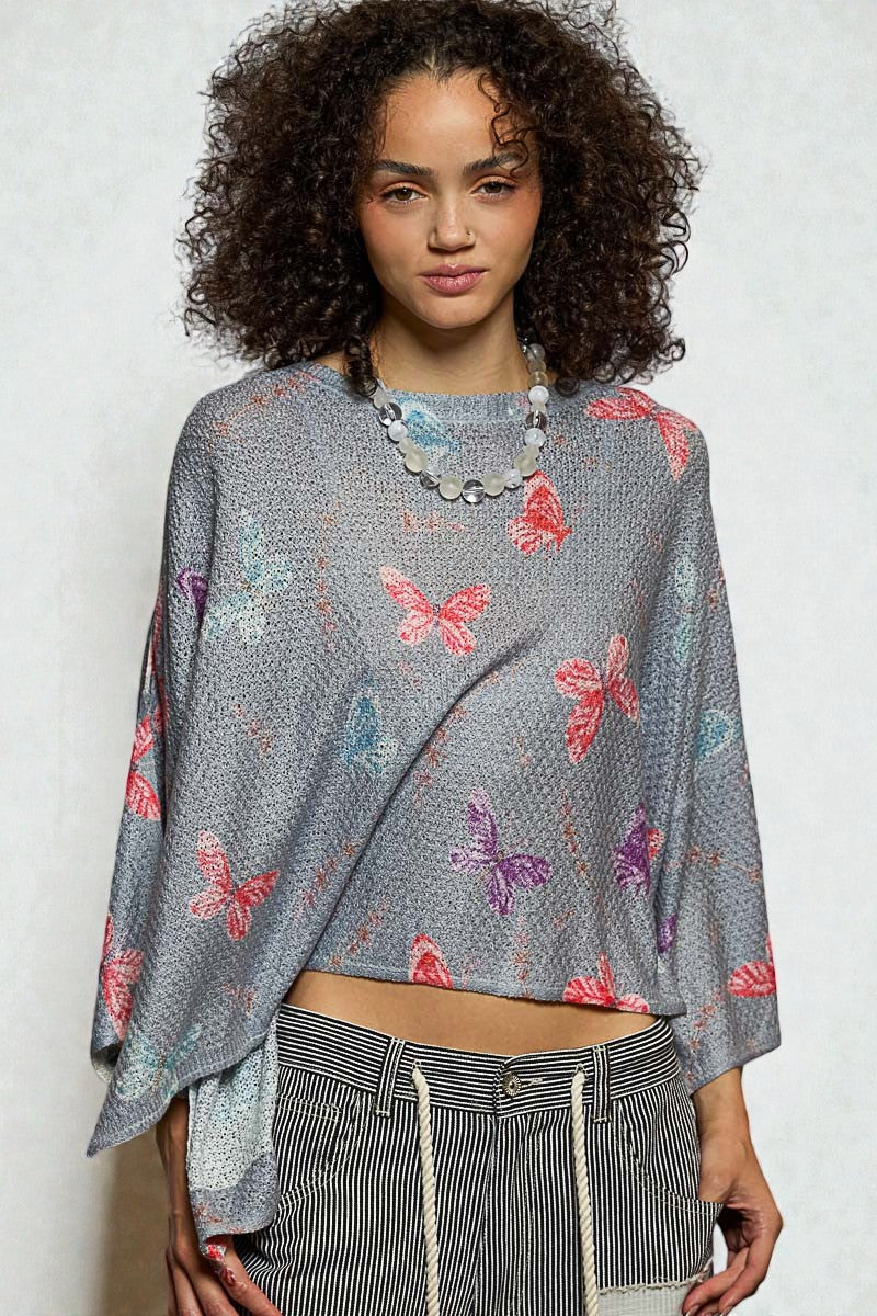 Woman wearing a gray sweater with butterfly patterns on a plain background