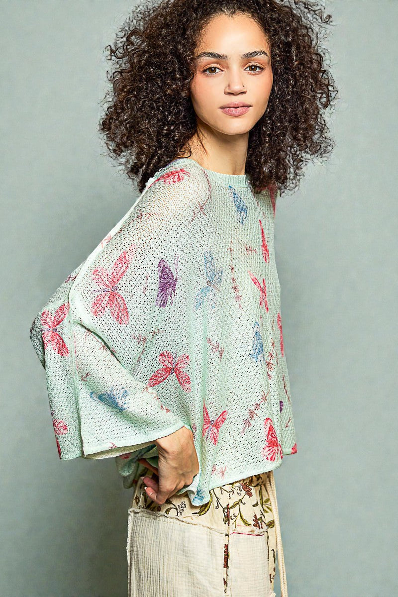 Woman wearing a light green sweater with butterfly patterns against a gray background