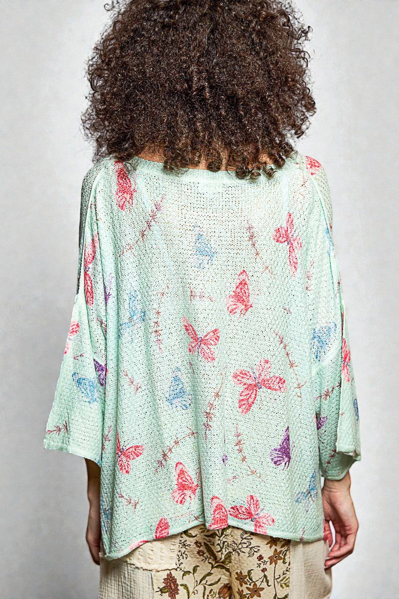 Person wearing a light green kimono-style garment with butterfly patterns on a plain background