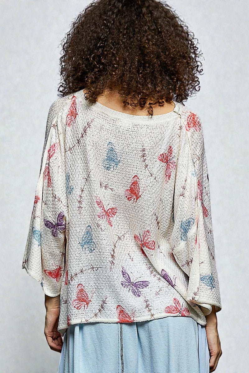 Person wearing a light-colored cardigan with butterfly pattern on a plain background