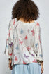 Person wearing a light-colored cardigan with butterfly pattern on a plain background
