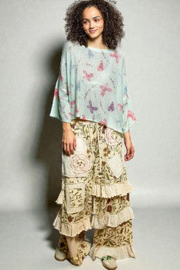 Woman wearing a light blue top with butterfly patterns and a floral skirt on a plain background