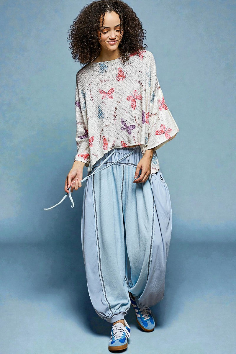 Woman wearing a butterfly-patterned top and light blue pants against a blue background