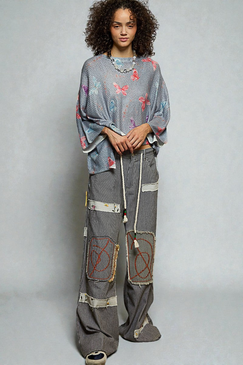 Person wearing a patterned sweater and patchwork pants on a plain background