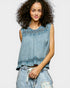Woman wearing a denim sleeveless top with ruffled details on a white background
