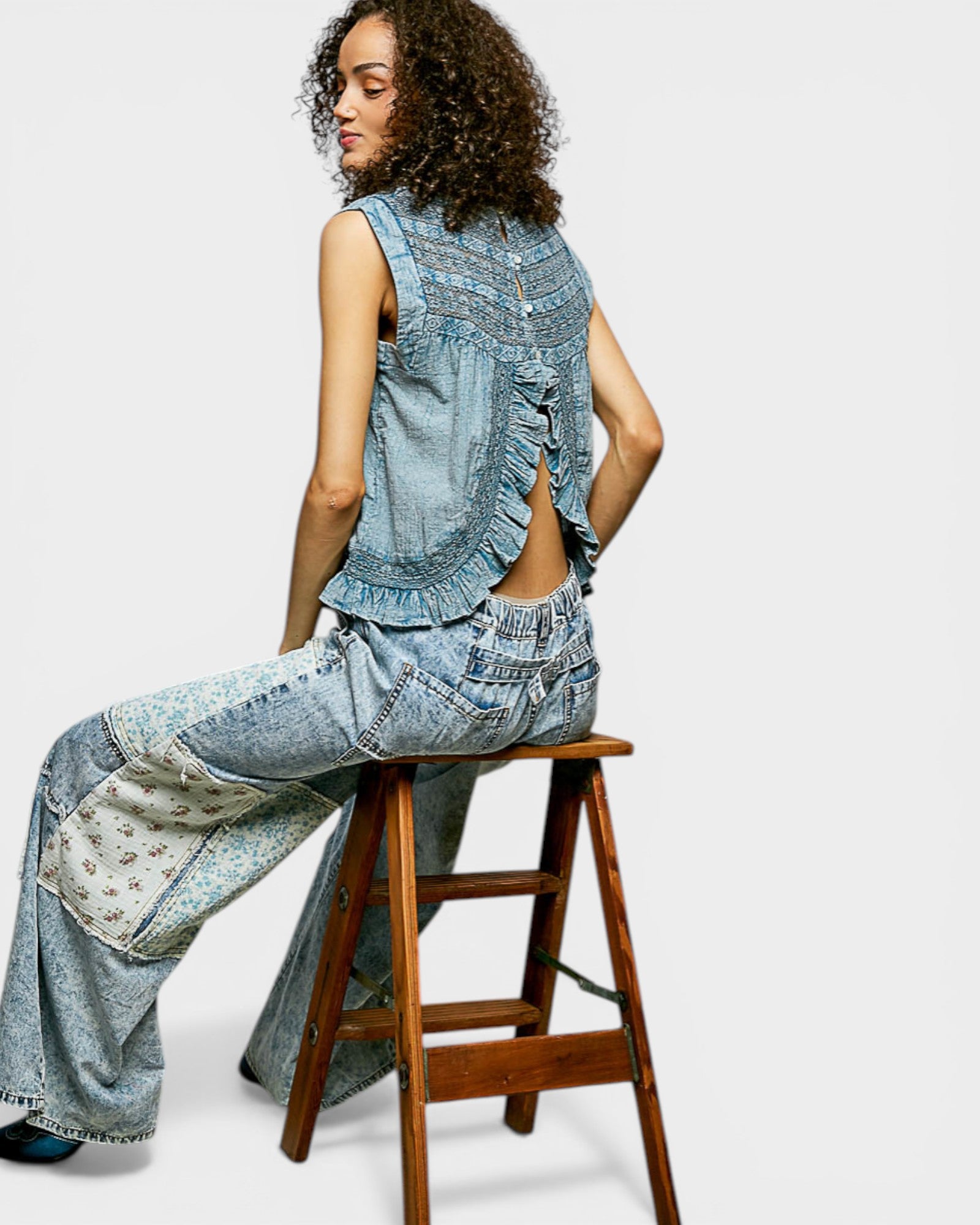 Person wearing a denim outfit sitting on a wooden stool against a white background