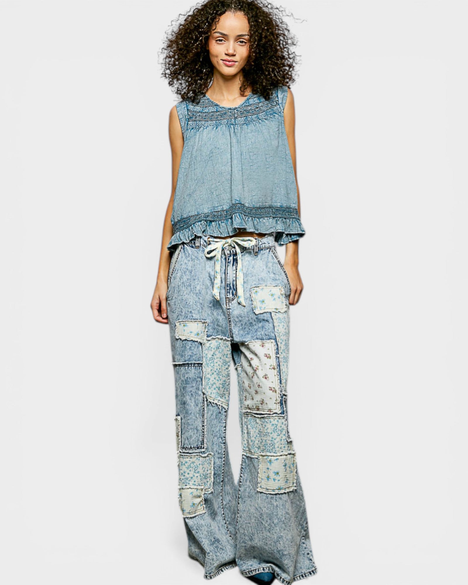 Woman wearing a denim sleeveless top and patchwork jeans on a white background