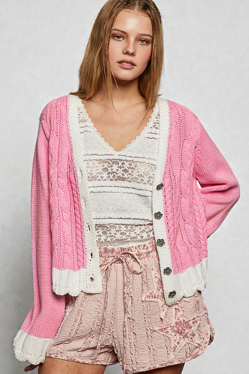 Woman wearing a pink cardigan over a white lace top and pink shorts on a light gray background