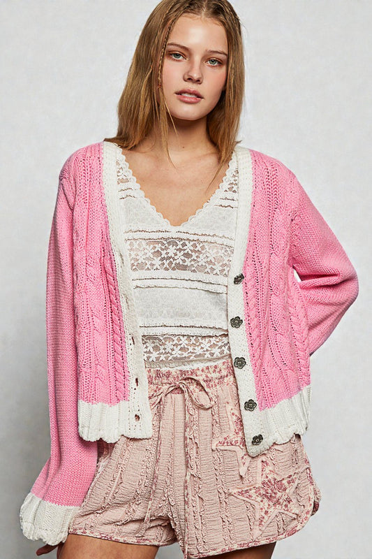 Woman wearing a pink cardigan over a white lace top and pink shorts on a light gray background