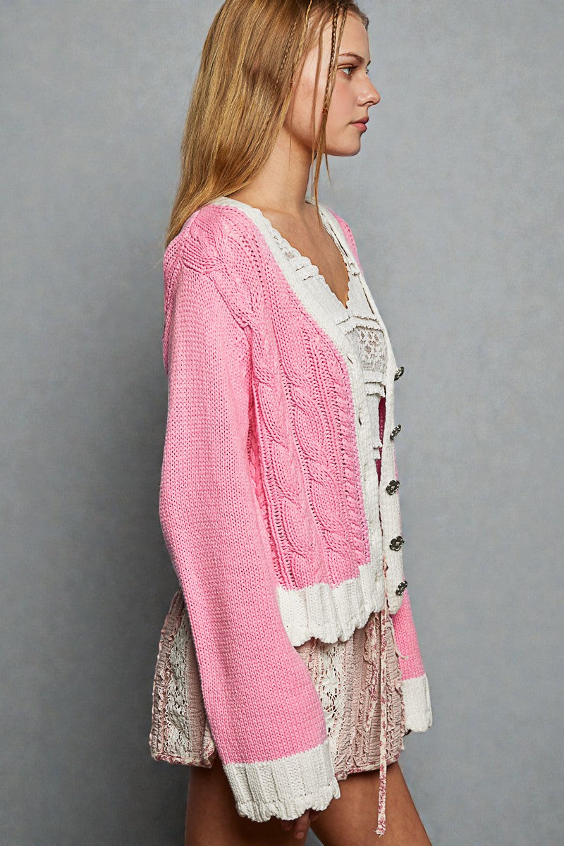 Woman wearing a pink cardigan over a white lace top and skirt on a gray background