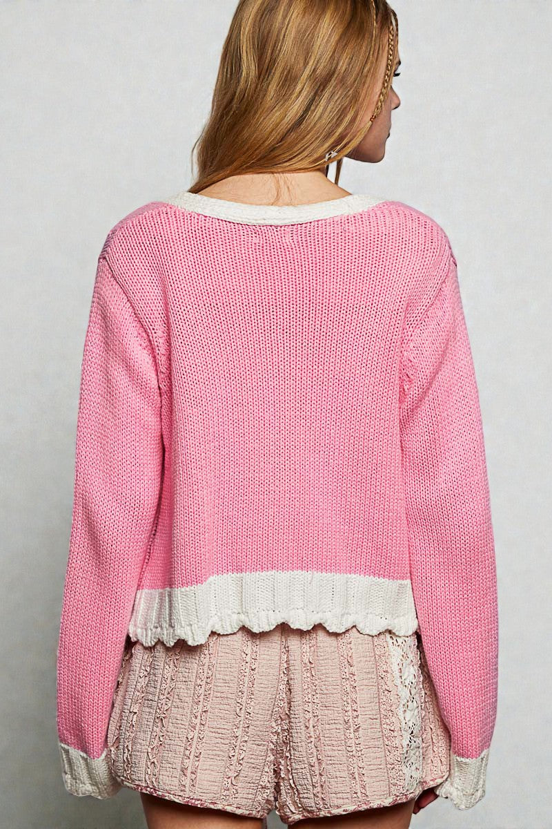 Person wearing a pink sweater with lace trim on a plain background