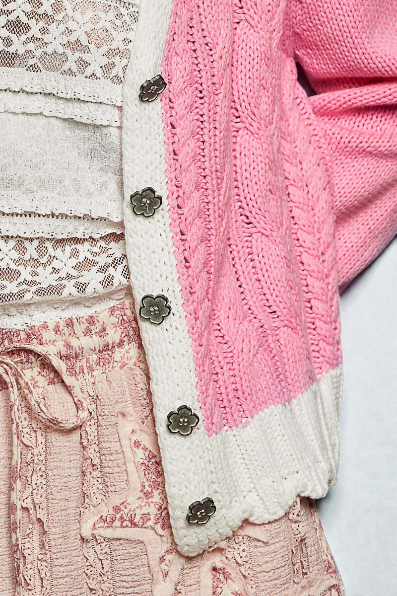 Close-up of a pink knitted cardigan with floral buttons on a white background