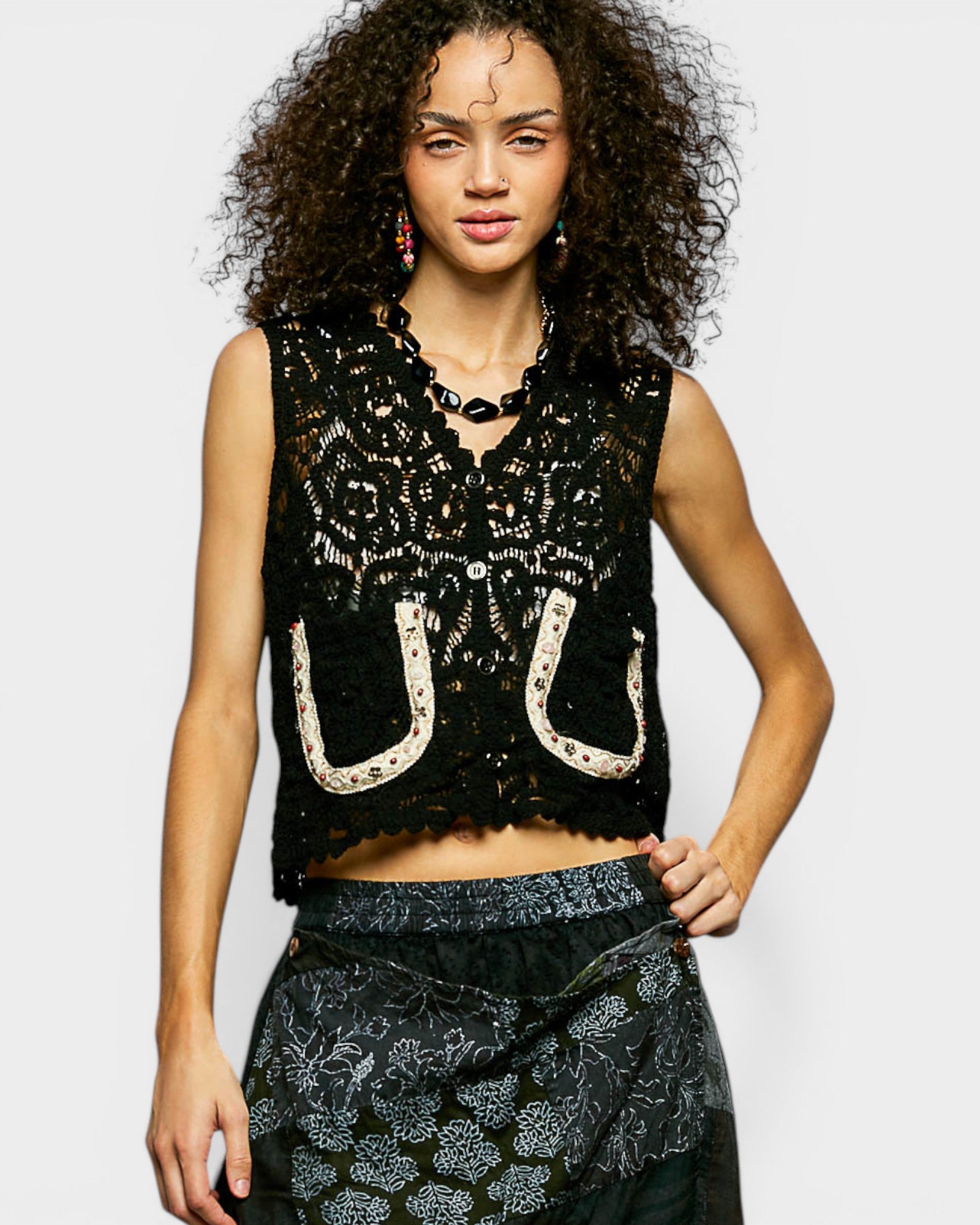 Woman wearing a black lace top with cut-out design on a plain background