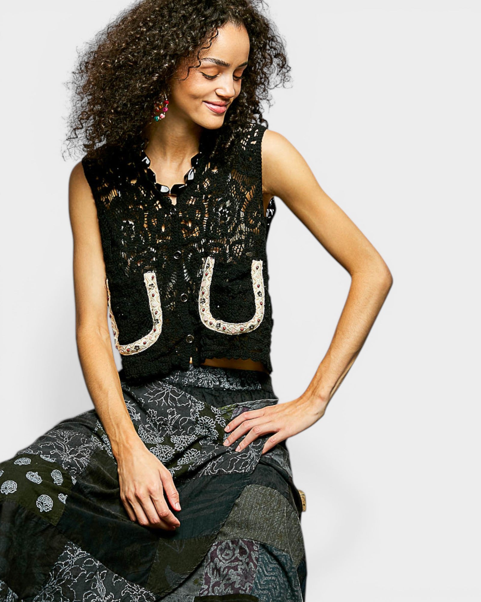 Woman wearing a black sleeveless top with white horseshoe designs on a plain background