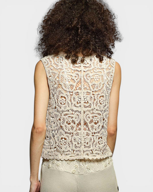 Person wearing a beige lace top against a plain background